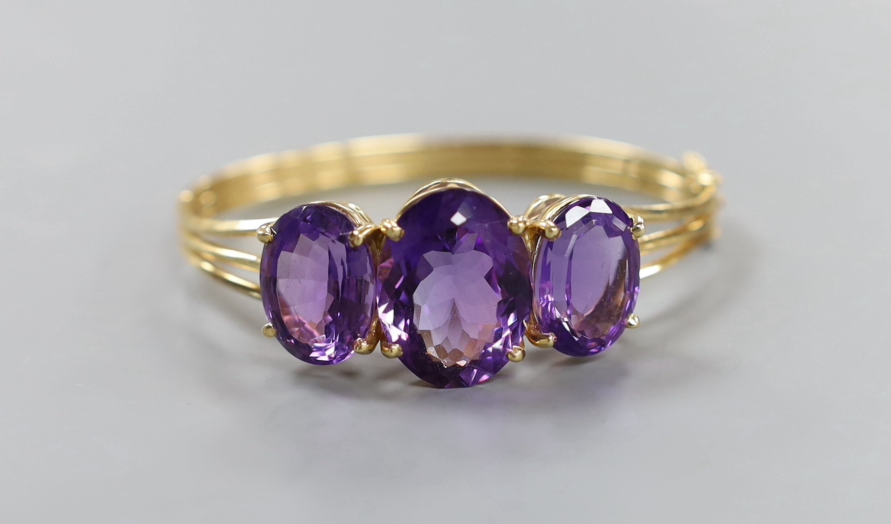 A modern 14k and three stone oval cut amethyst set hinged bangle, interior diameter 54mm, gross weight 24.8 grams.